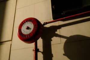 A red fire alarm bell with sprinkler system shadow on exterior wall in Hong Kong.