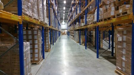 Interior view of a large warehouse aisle lined with stacks of organized cardboard boxes.